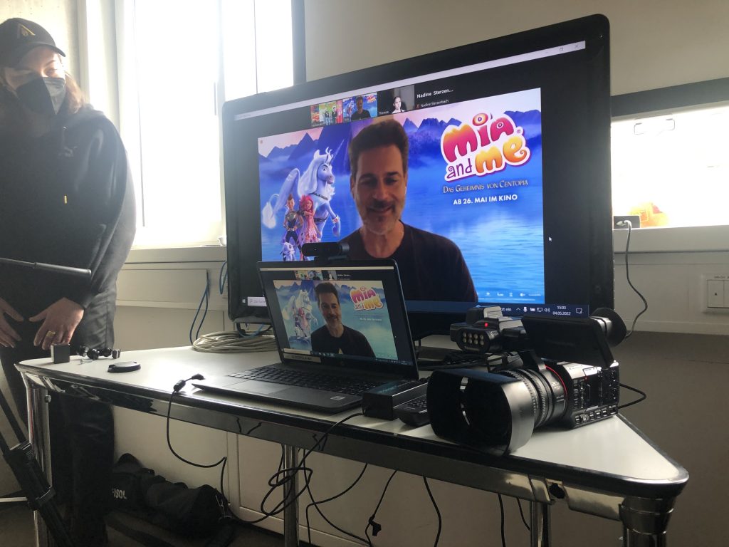 Rick Kavanians Videokachel auf einem Fernseher und Laptop, daneben eine große Kamera - Text: Beim Videotelefonat mit Rick kam jede Menge Elektronik zum Einsatz
