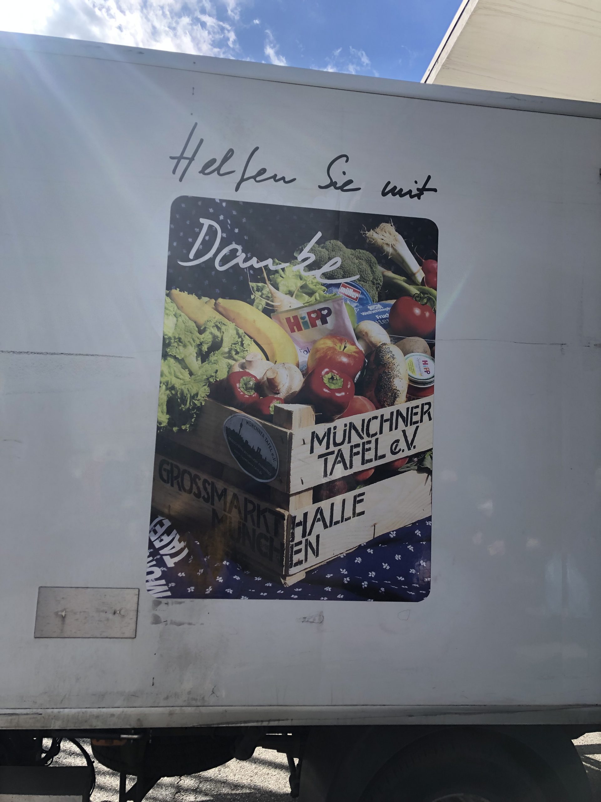 Ein Laster der Münchner Tafel, auf ihm ist ein Bild von Lebensmitteln mit dem Text "Helfen sie mit"